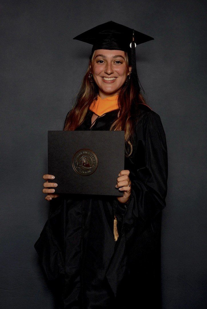 Camila at her graduation, holding her Master's diploma
